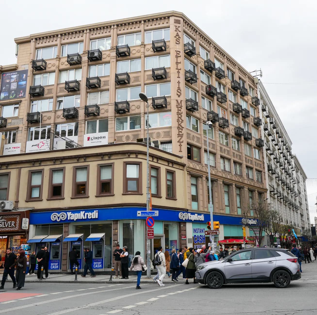 Crowded street intersection in İstanbul near Kaş Etiler İş Merkezi with visible pedestrians and architecture.