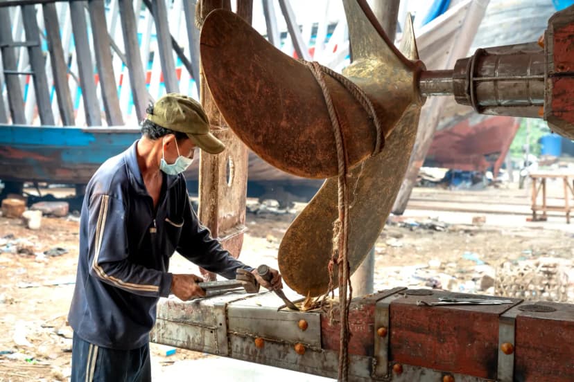 A man fixing a large ship turbine in an outdoor shipyard, showcasing industrial repair work.