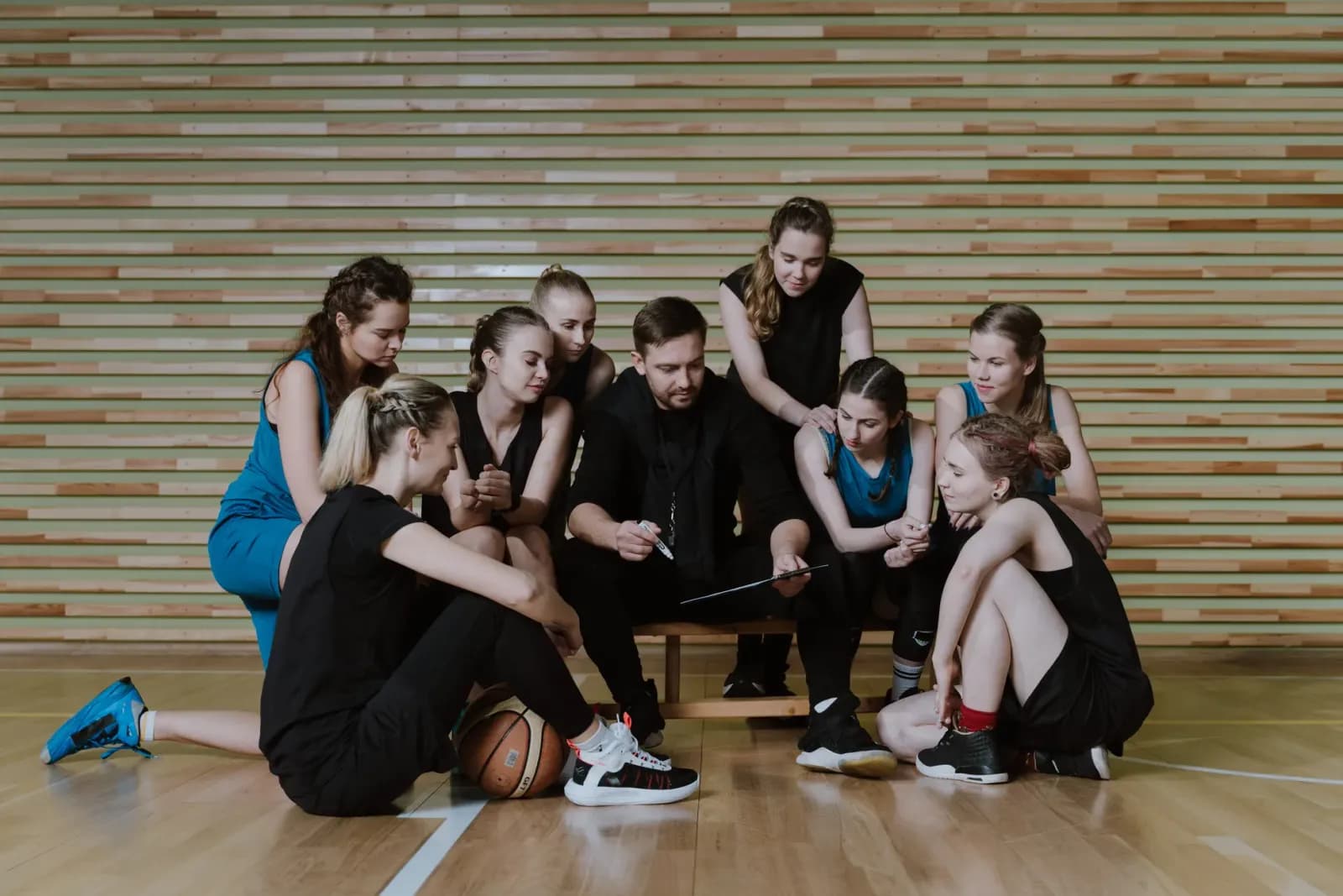sahada oyunclarına taktik veren basketbol antrenörü, masada basketbol stratejisi inceleyen antrenör, spor salonunda teknik analiz toplantısı