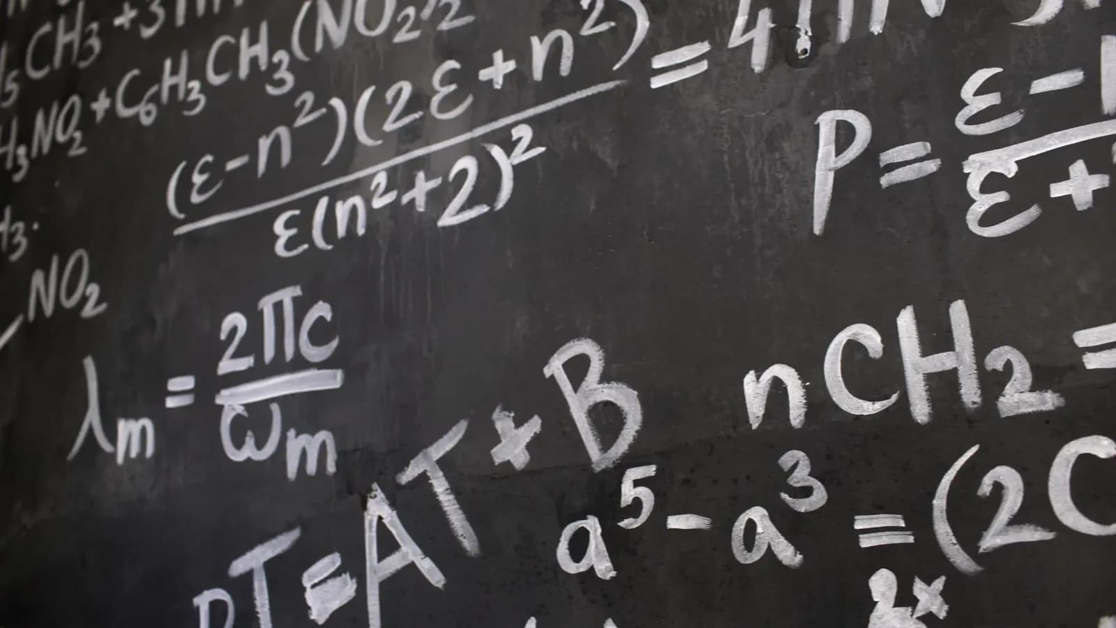 bilgisayar başında veri analizi yapan matematikçi, tahtada karmaşık denklemler üzerinde uzman, akademik çalışma ortamı