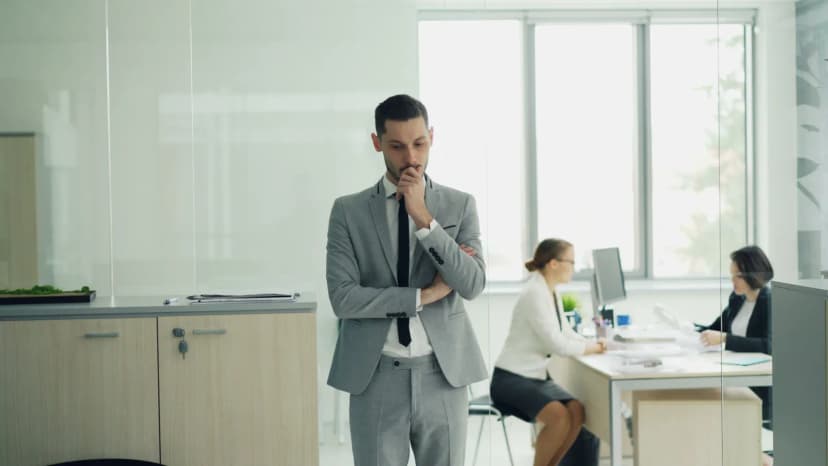 Thoughtful businessman in a modern office setting with colleagues working in the background.