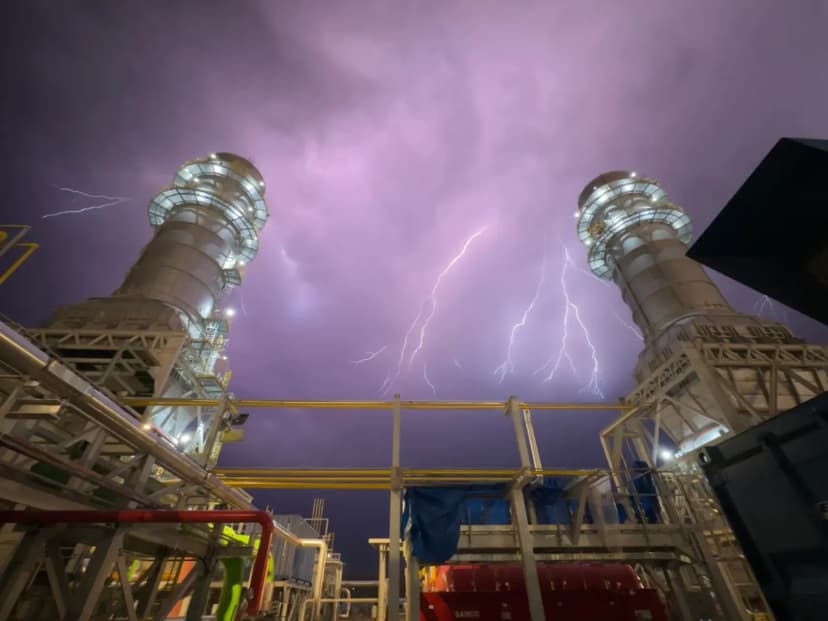 Power plant towers against stormy sky with lightning striking, showcasing industrial might.