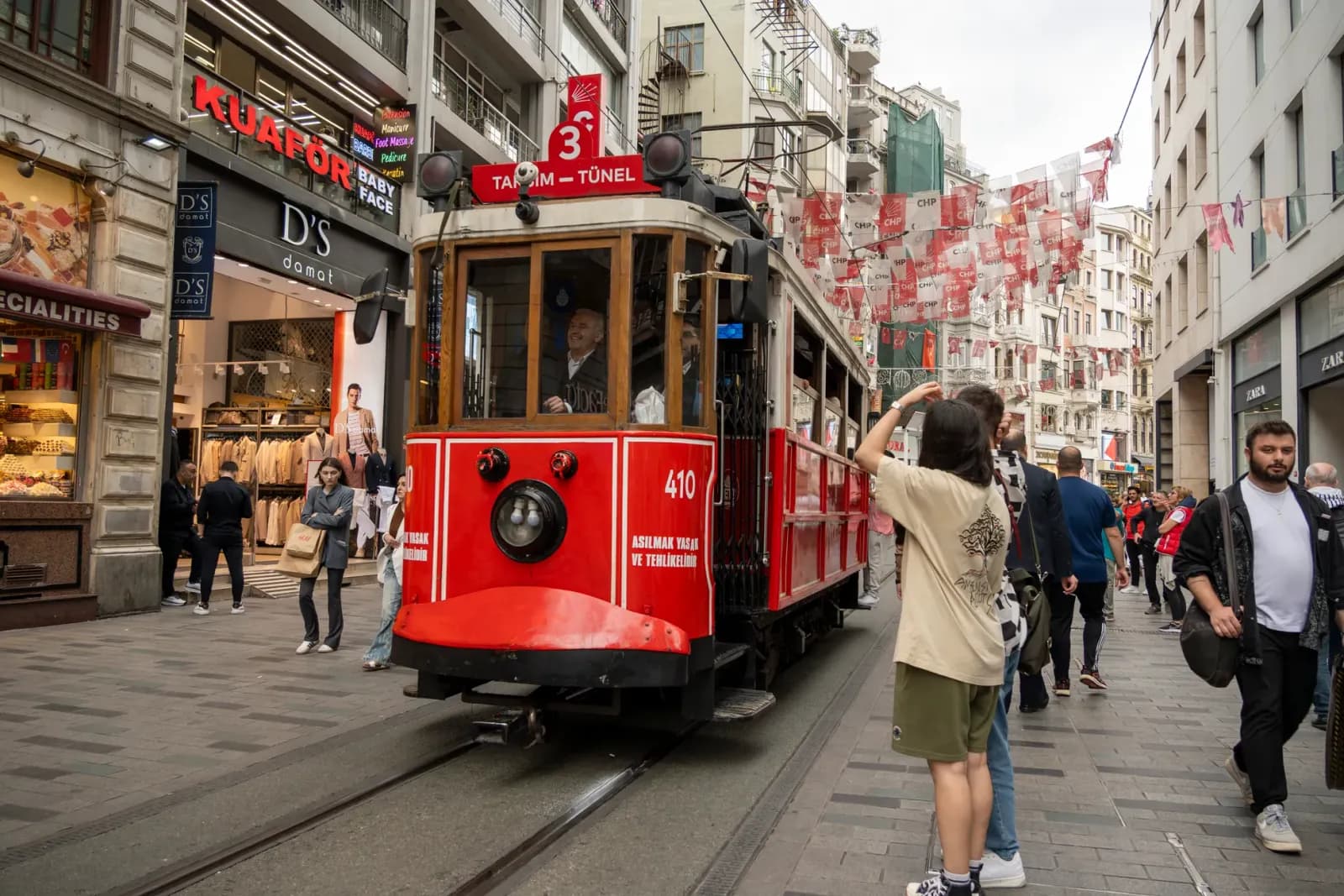 Red tram traversing vibrant pedestrian street in Istanbul, teeming with lively urban scenes and local shops.