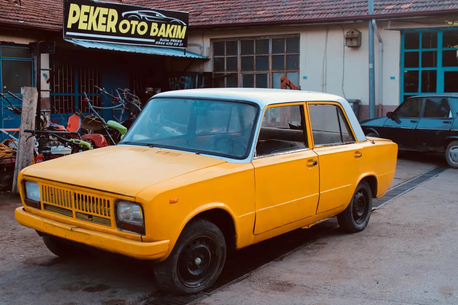A classic yellow car parked outside a local auto repair shop with tools visible.
