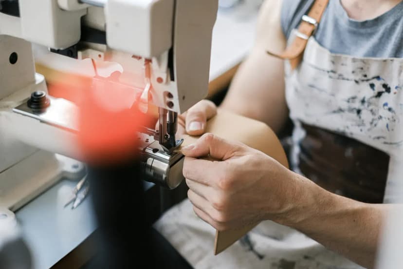 Close-up of a craftsman sewing leather with an industrial machine, showcasing precision work.
