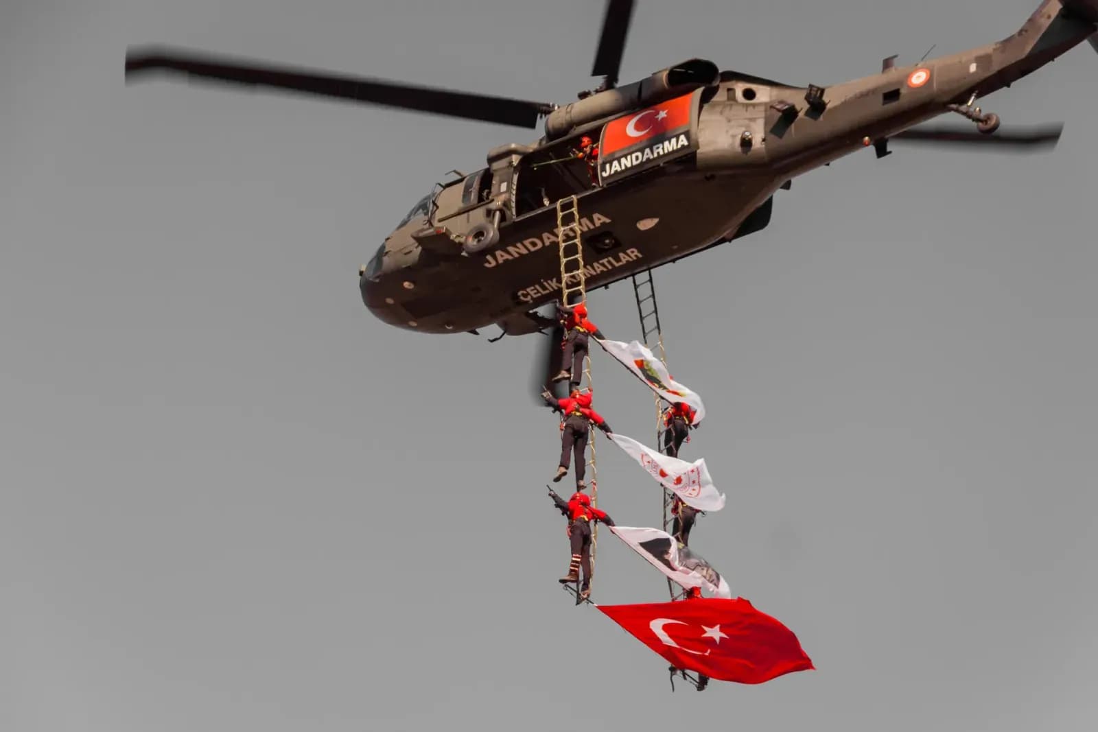 Turkish Jandarma helicopter performs aerial display with flag and personnel.