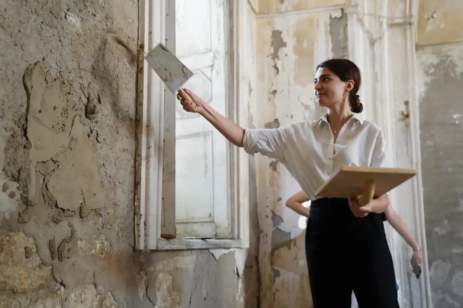 A woman in a white shirt renovating an old interior by applying plaster to walls.