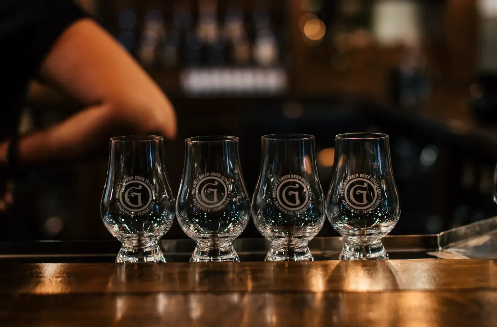 Four empty Glencairn glasses aligned on a bar counter in a dimly lit setting.