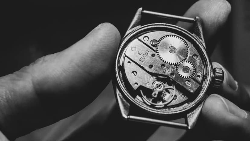 Black and white close-up of a vintage watch mechanism held in hand, showcasing intricate gears.