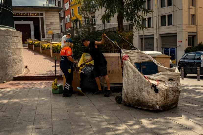 Two sanitation workers collecting waste on a sunny day in the city.