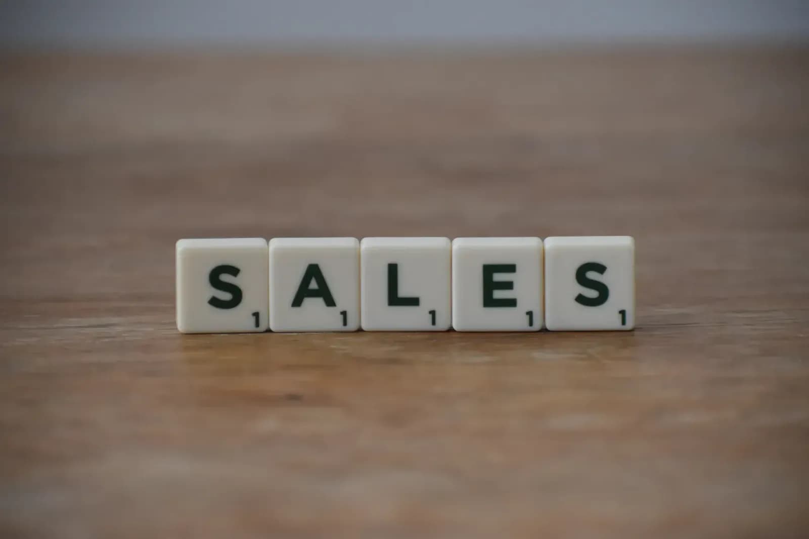 Scrabble tiles spelling 'sales' on a wooden table, emphasizing business and marketing.